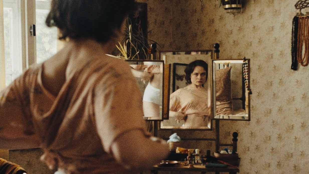 A young woman adjusts her crop top in front of a mirror.